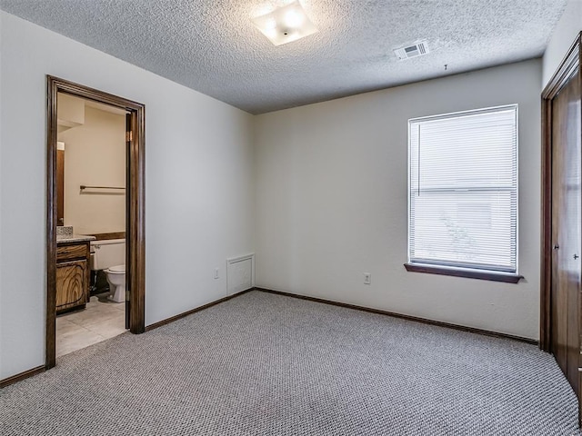 unfurnished bedroom with connected bathroom, a textured ceiling, visible vents, light carpet, and baseboards