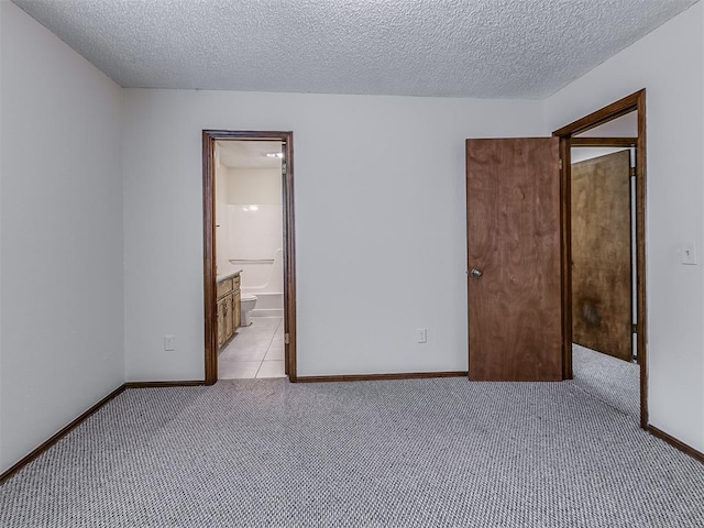unfurnished bedroom featuring a textured ceiling, light colored carpet, baseboards, and connected bathroom