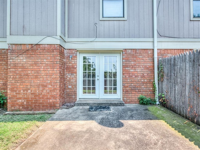 doorway to property featuring brick siding, french doors, and fence