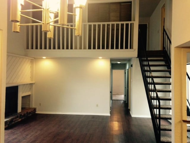 unfurnished living room with baseboards, a high ceiling, a brick fireplace, dark wood-style floors, and stairs