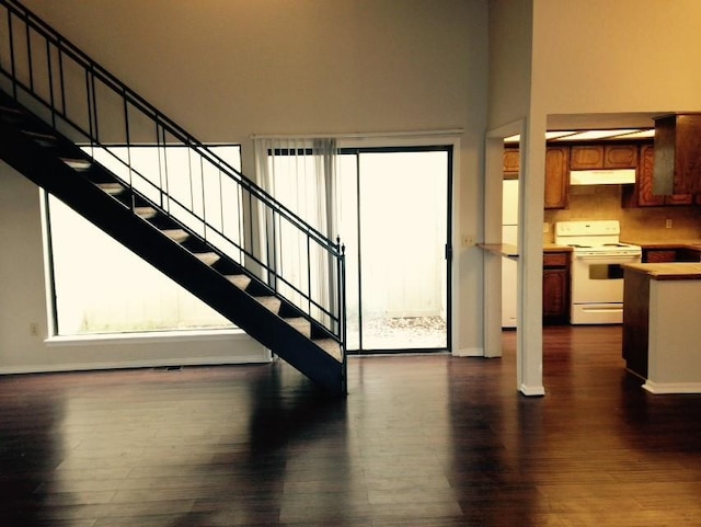 stairway featuring wood finished floors, a towering ceiling, and baseboards