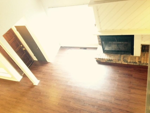 unfurnished living room with a brick fireplace, visible vents, and wood finished floors