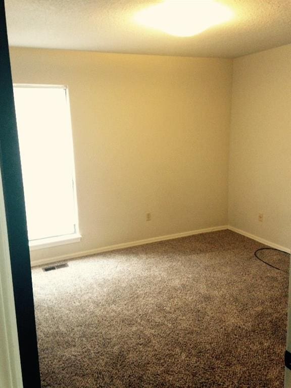 carpeted spare room featuring visible vents and baseboards
