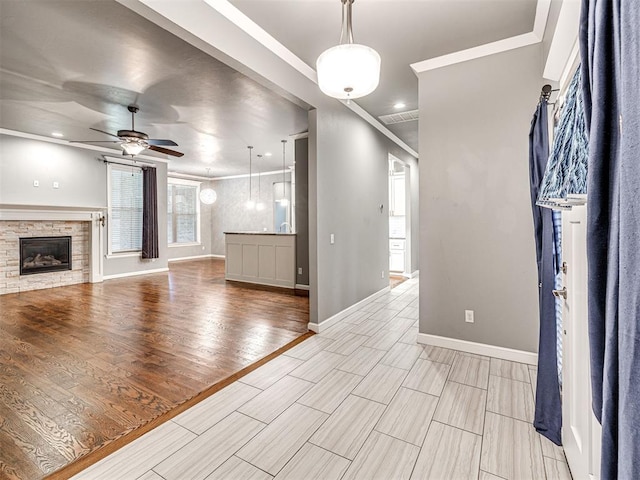 unfurnished living room featuring baseboards, a stone fireplace, visible vents, ceiling fan, and light wood finished floors
