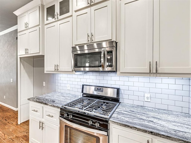 kitchen with baseboards, light wood-style floors, light stone countertops, decorative backsplash, and stainless steel appliances