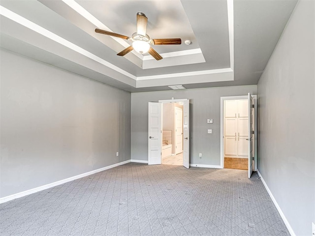 unfurnished bedroom with ensuite bathroom, a ceiling fan, carpet flooring, a raised ceiling, and baseboards