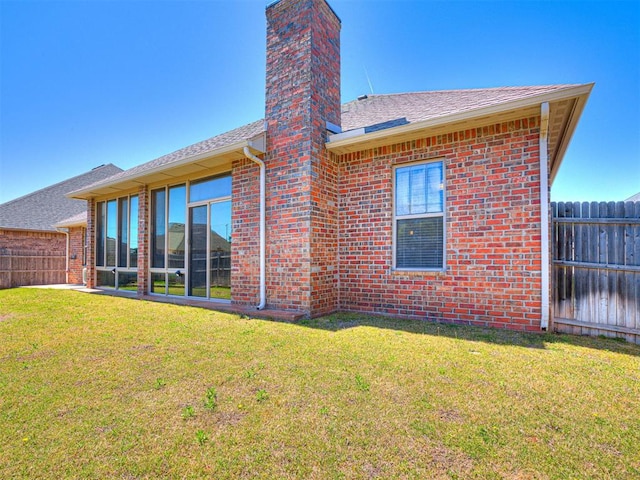 back of property featuring a shingled roof, a yard, a chimney, fence, and brick siding