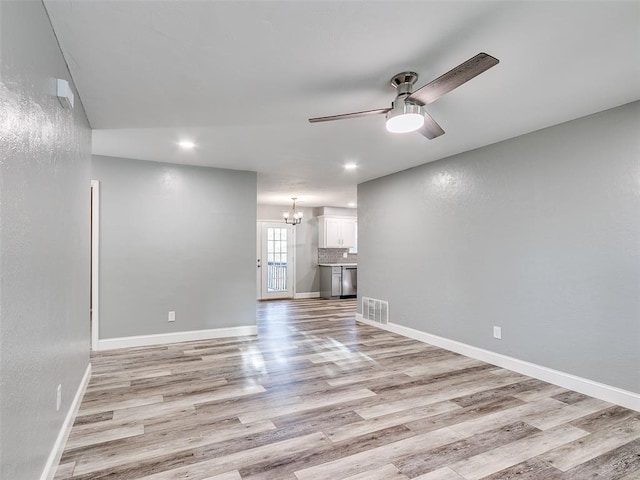 unfurnished living room featuring ceiling fan with notable chandelier, light wood finished floors, baseboards, and visible vents