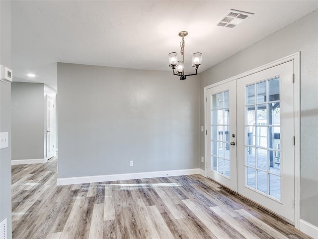 unfurnished dining area with visible vents, baseboards, light wood-type flooring, a chandelier, and french doors