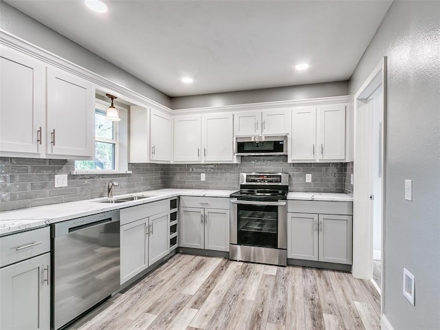kitchen with a sink, light wood-type flooring, gray cabinetry, stainless steel appliances, and backsplash