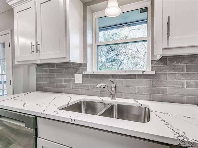 kitchen with tasteful backsplash, dishwasher, a sink, and white cabinetry