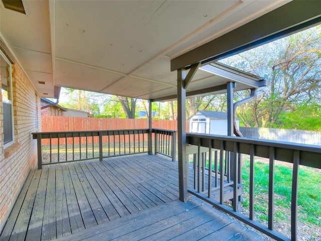 wooden terrace featuring a storage shed, fence, and an outbuilding