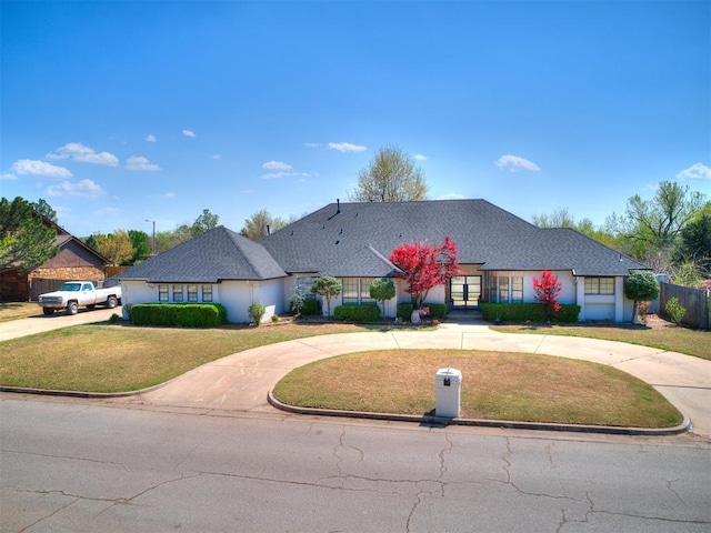 ranch-style home with curved driveway, fence, and a front lawn