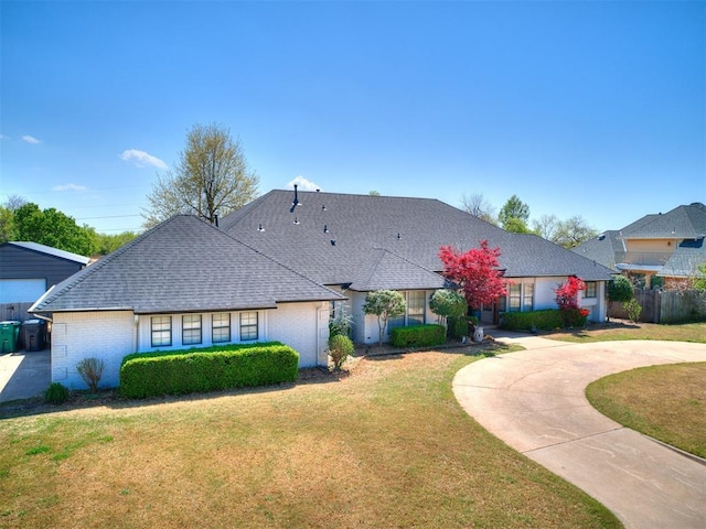 view of front of home with roof with shingles, a front yard, and brick siding