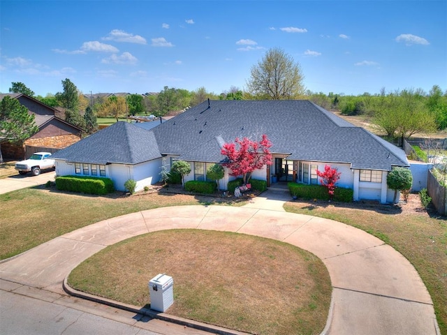 ranch-style home featuring a front lawn, a shingled roof, and curved driveway