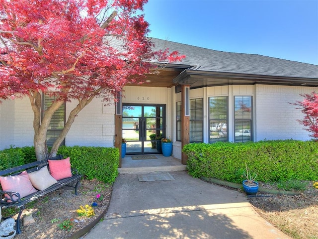 entrance to property with brick siding, french doors, and a shingled roof