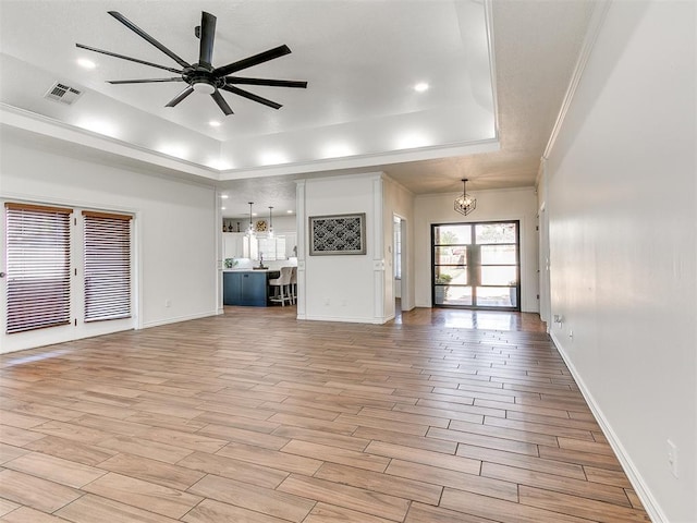 unfurnished living room with visible vents, a raised ceiling, light wood-style floors, and ceiling fan with notable chandelier