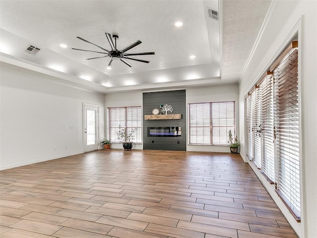 unfurnished living room with a tray ceiling, wood finished floors, a ceiling fan, and visible vents