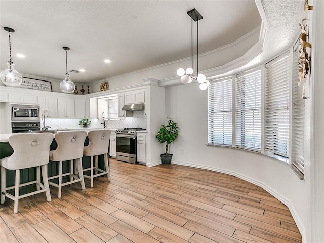 kitchen with crown molding, under cabinet range hood, light countertops, stainless steel appliances, and decorative backsplash