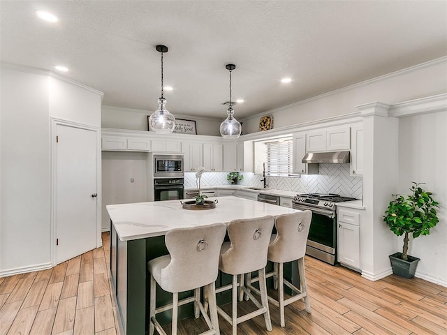 kitchen with light wood-style flooring, a kitchen island, appliances with stainless steel finishes, under cabinet range hood, and decorative backsplash
