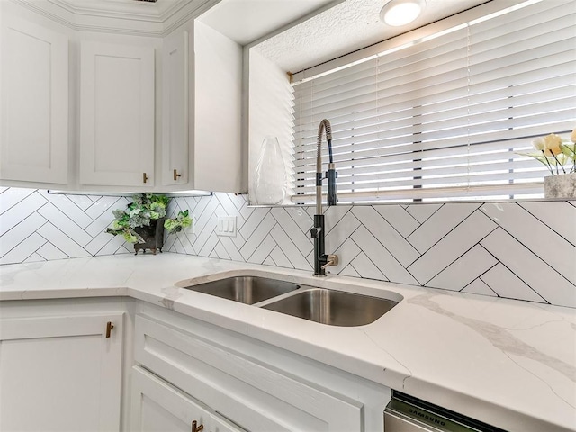 kitchen featuring light stone counters, white cabinetry, backsplash, stainless steel dishwasher, and a sink