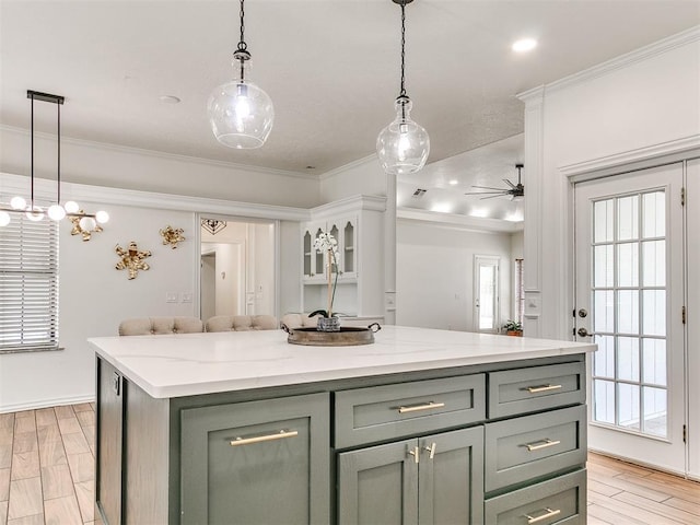 kitchen featuring crown molding, pendant lighting, a ceiling fan, a kitchen island, and light stone counters