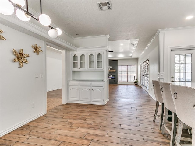 interior space featuring light wood-style flooring, ornamental molding, white cabinetry, and visible vents