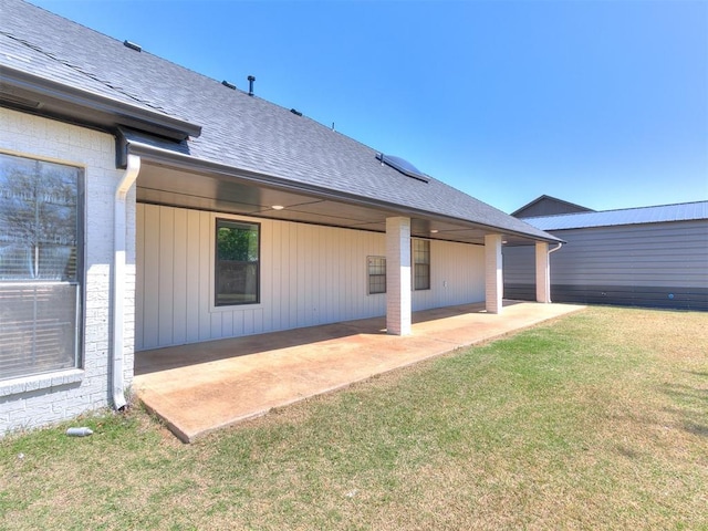 back of house featuring a shingled roof, a patio, and a lawn