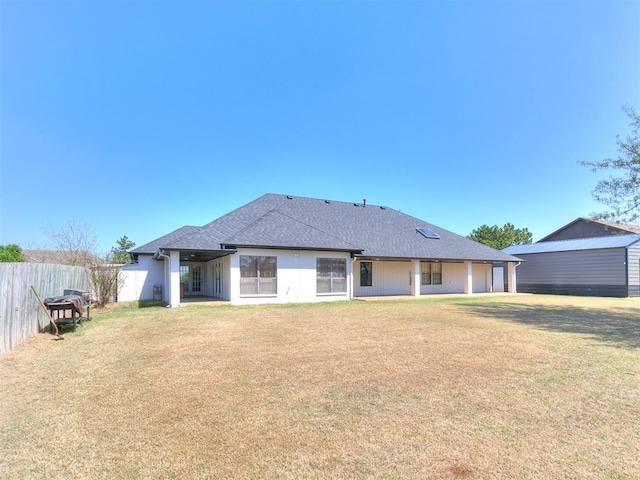 back of house featuring roof with shingles, fence, and a lawn