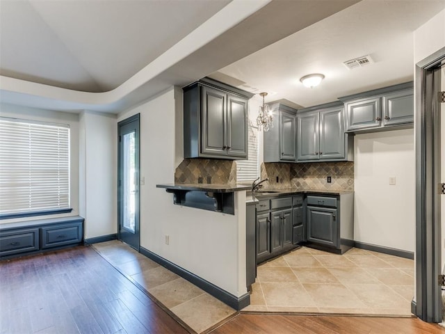 15213 Wilford Way, Edmond, OK 73013 - kitchen featuring visible vents, dark countertops, gray cabinetry, decorative backsplash, and a breakfast bar area