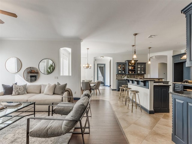 15213 Wilford Way, Edmond, OK 73013 - living room featuring arched walkways, ceiling fan with notable chandelier, crown molding, and visible vents