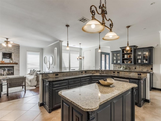 15213 Wilford Way, Edmond, OK 73013 - kitchen with ceiling fan, a stone fireplace, visible vents, a kitchen island, and a sink