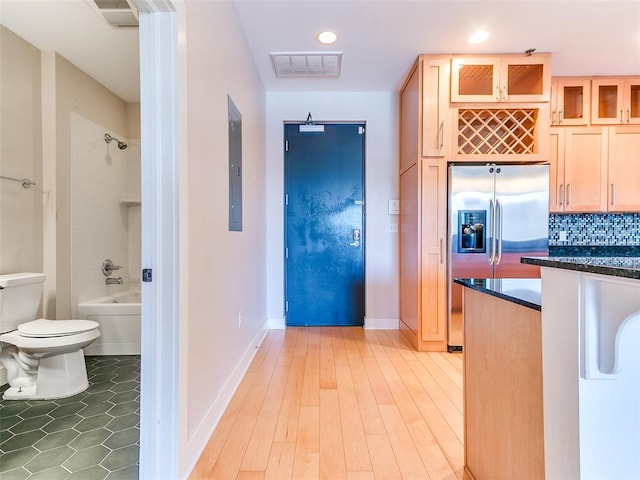 kitchen with dark stone counters, tasteful backsplash, glass insert cabinets, visible vents, and stainless steel fridge with ice dispenser