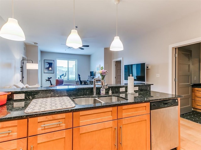 kitchen featuring a sink, light wood-style floors, dark stone countertops, stainless steel dishwasher, and open floor plan