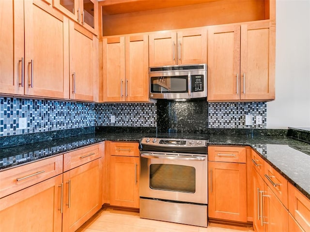 kitchen with glass insert cabinets, dark stone countertops, appliances with stainless steel finishes, and decorative backsplash
