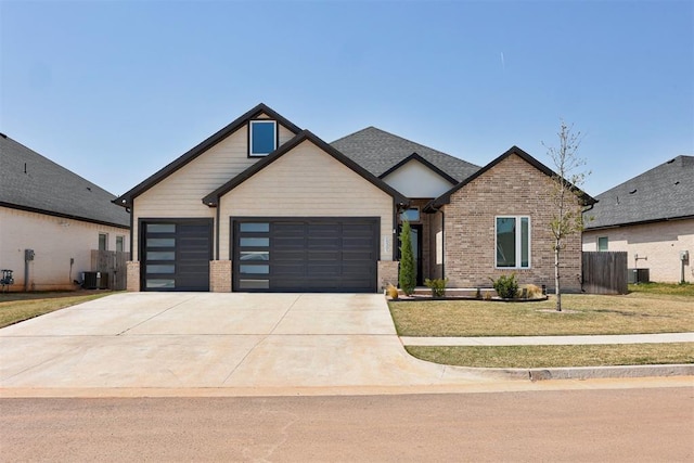 craftsman inspired home with concrete driveway, central air condition unit, an attached garage, a front yard, and brick siding