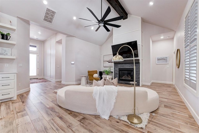 living area with visible vents, a ceiling fan, a glass covered fireplace, and light wood finished floors