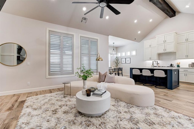 living room featuring light wood-style flooring, a ceiling fan, visible vents, baseboards, and beam ceiling