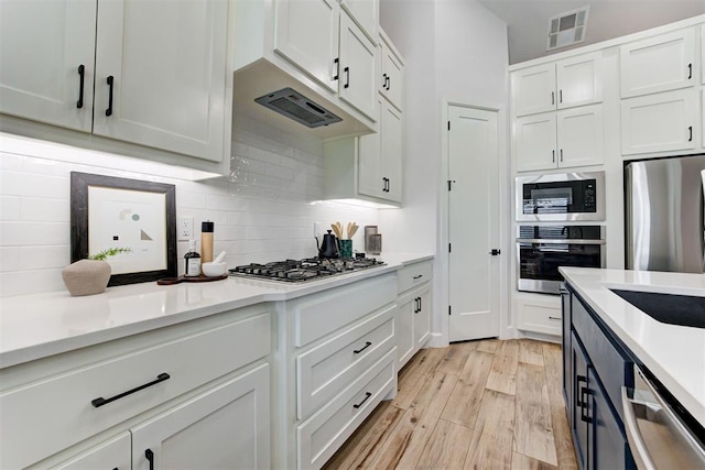kitchen featuring backsplash, white cabinets, light wood-style floors, visible vents, and stainless steel appliances