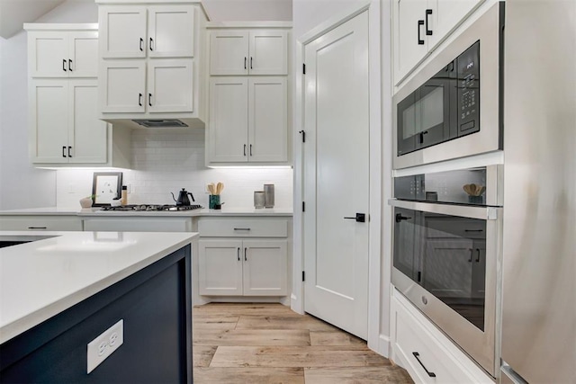 kitchen with light wood-style floors, oven, built in microwave, and white cabinetry