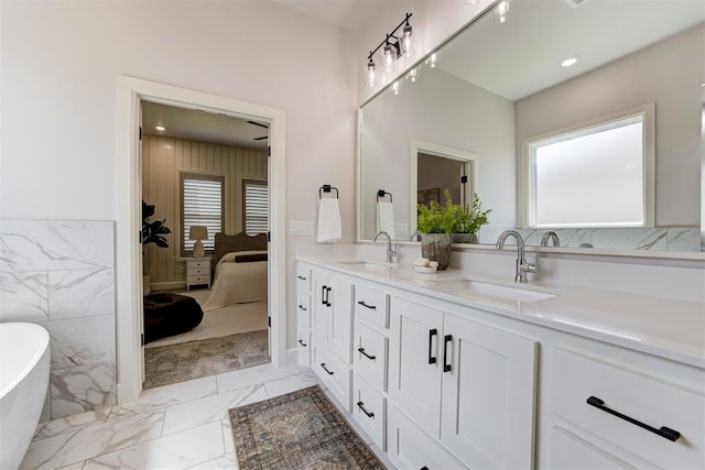 ensuite bathroom with a sink, a freestanding bath, marble finish floor, and double vanity