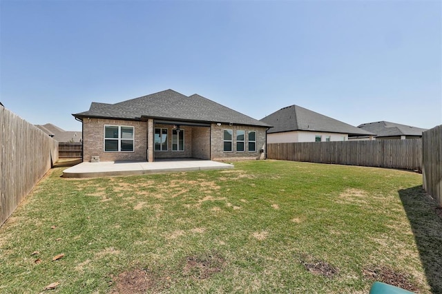 rear view of house featuring a patio area, a lawn, a fenced backyard, brick siding, and roof with shingles
