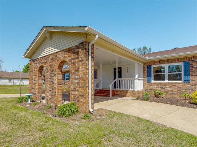 view of side of home with a yard, brick siding, and covered porch