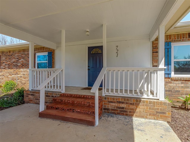 doorway to property with covered porch and brick siding