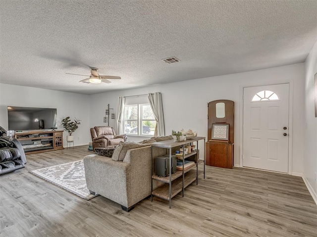 living area with visible vents, a textured ceiling, light wood finished floors, and a ceiling fan