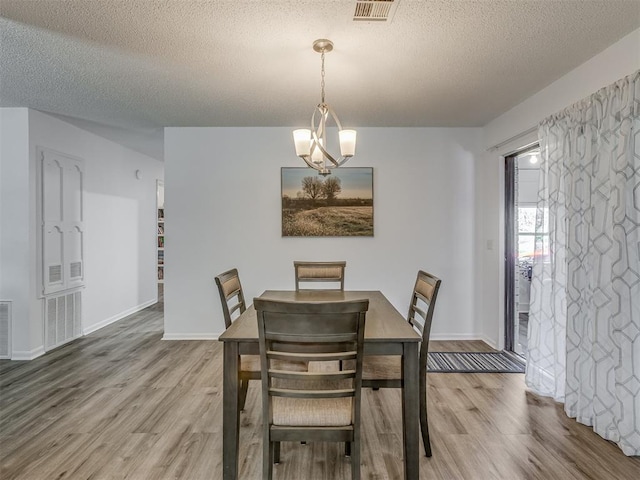 dining room featuring visible vents, baseboards, wood finished floors, and a textured ceiling