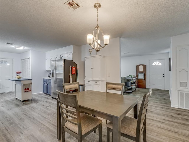 dining room featuring light wood-type flooring, visible vents, a textured ceiling, and an inviting chandelier