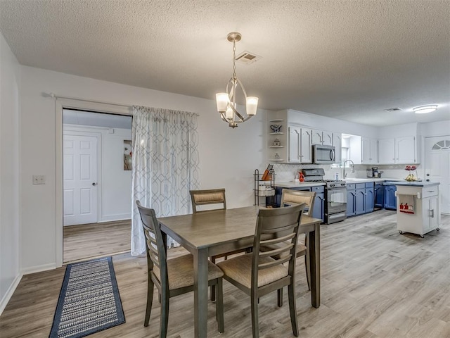 dining space featuring a textured ceiling, light wood finished floors, baseboards, and visible vents