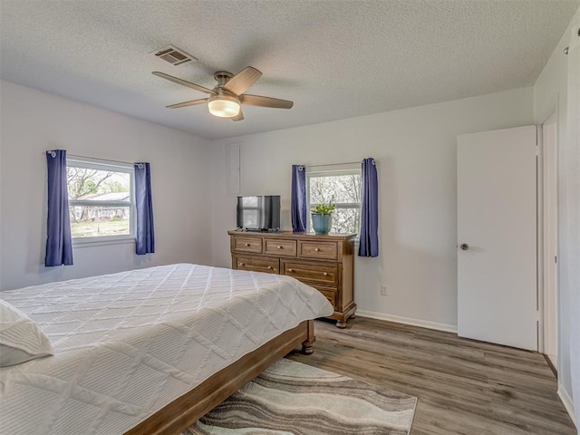 bedroom with wood finished floors, ceiling fan, multiple windows, and visible vents