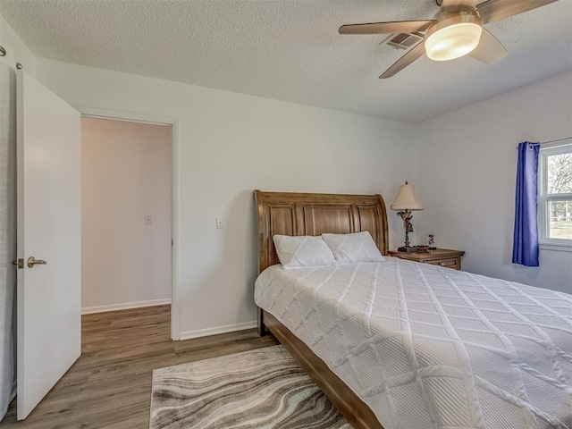 bedroom featuring visible vents, baseboards, a ceiling fan, a textured ceiling, and wood finished floors